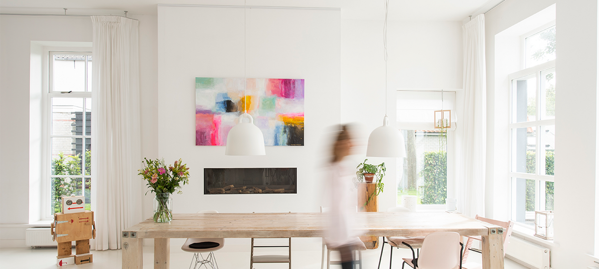 Lichte, moderne woonkamer met kleurrijk schilderij boven de haard, opgehangen met een Artiteq schilderij ophangsysteem en ophangdraden