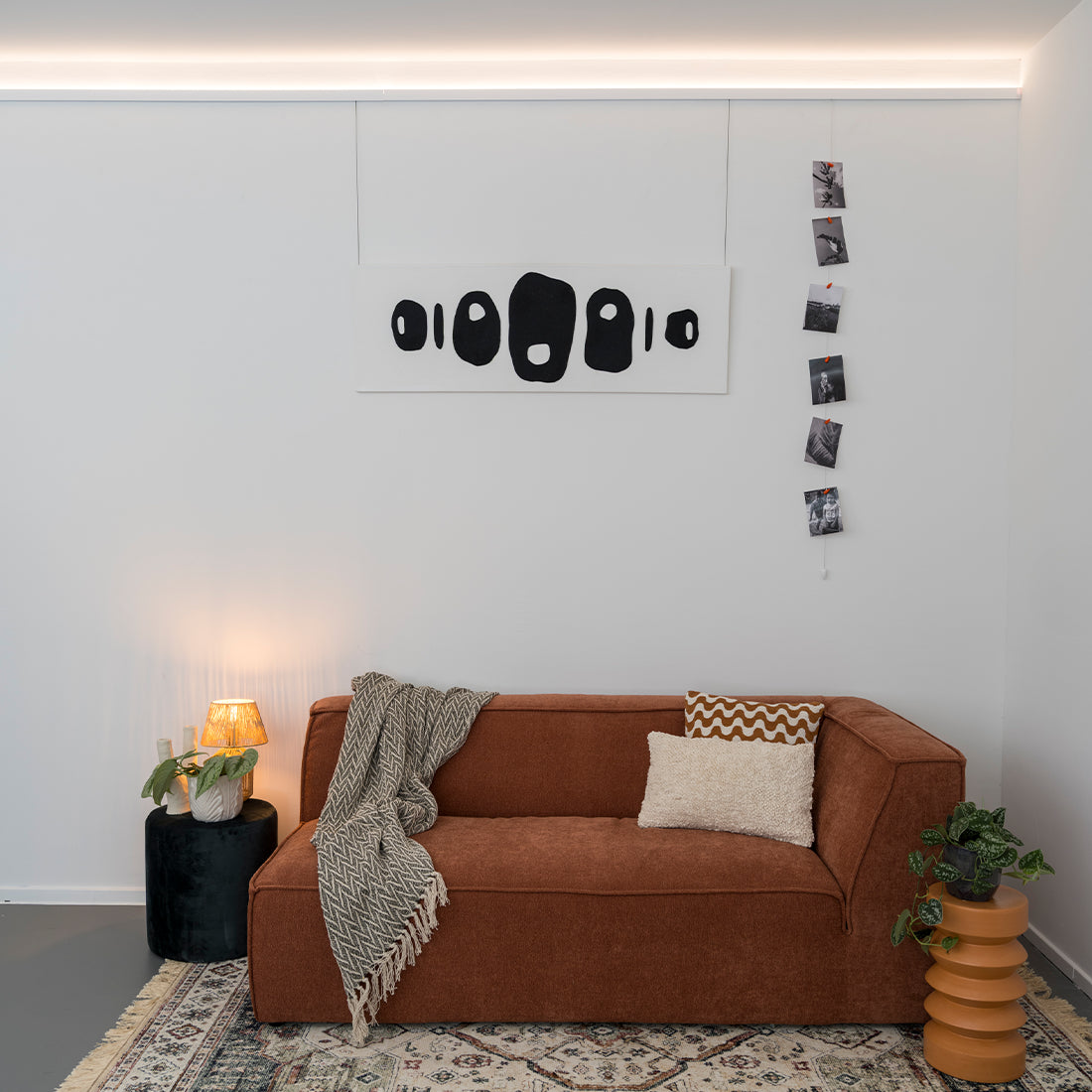 Groot schilderij aan LED verlichtingsrail met rode bank